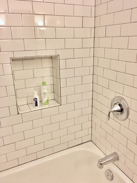 One corner of the shower in question, freshly tiled in bone white subway tile.